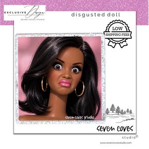 May include: A doll with dark skin, shoulder-length black hair, and gold hoop earrings. The doll has a facial expression of disgust with wide eyes and pursed pink lips. The image includes text reading Exclusive Design, Seven Coves Studio, and Disgusted Doll.