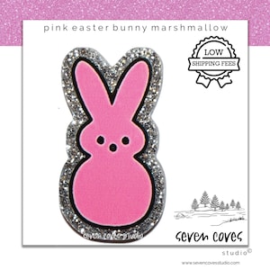 May include: Pink glitter Easter bunny marshmallow peep with silver glitter trim.  The bunny is shaped like a traditional marshmallow peep with a pink body and white eyes.