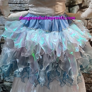 May include: A layered tulle skirt with iridescent fabric and a blue denim waistband. The skirt has a ruffled design and is perfect for a whimsical or fairy-themed outfit.
