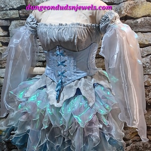May include: A fantasy-themed dress with a light blue corset and a layered skirt. The dress features sheer, flowing sleeves and a bodice with blue lacing. The skirt has iridescent accents, and the dress is displayed on a mannequin.