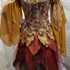 K&ouml;nnte beinhalten: Ein mehrlagiges, herbstliches Kleid mit einem floralen Oberteil, einem gold- und braunen, gerafften Rock und durchsichtigen gelben &Auml;rmeln. Das Kleid hat einen wei&szlig;en Unterrock.