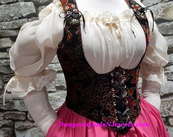 May include: A black velvet corset with gold embroidery and red accents. The corset has a lace-up front and is worn over a white peasant blouse with puffed sleeves and a lace trim. The corset is paired with a pink skirt.
