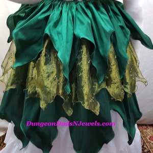 K&ouml;nnte beinhalten: Ein gr&uuml;ner Rock mit mehreren Lagen gekr&auml;uselten Stoffes. Die unterste Schicht ist ein durchsichtiger gr&uuml;ner Stoff mit goldenem Muster. Der Rock hat eine Website-Adresse, "DungeonDudsNJewels.com", auf der Vorderseite aufgedruckt.