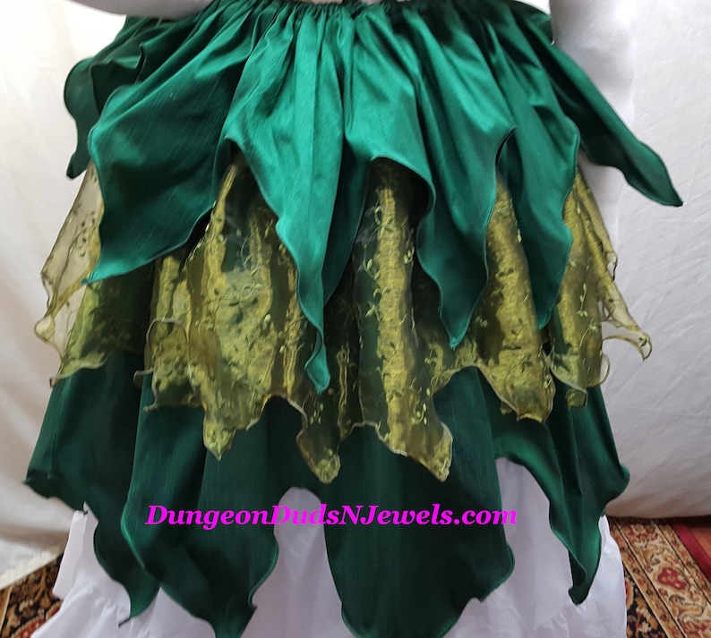 K&ouml;nnte beinhalten: Ein gr&uuml;ner Rock mit mehreren Lagen gekr&auml;uselten Stoffes. Die unterste Schicht ist ein durchsichtiger gr&uuml;ner Stoff mit goldenem Muster. Der Rock hat eine Website-Adresse, "DungeonDudsNJewels.com", auf der Vorderseite aufgedruckt.