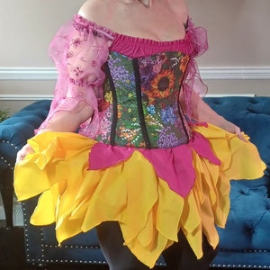 May include: A woman wearing a pink and yellow floral corset with a matching yellow and pink ruffled skirt. She is wearing black leggings and pink sneakers. The text "dungeondudsjewels.com" is visible in the bottom of the image.