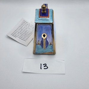 May include: A rectangular, hand-painted decorative box with a nautical theme. The box features a blue and gold color scheme with a sailboat design. The lid has a gold knob. A tag with text is attached.