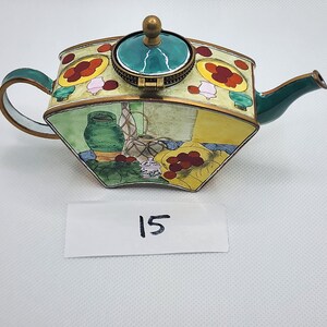 May include: A green and gold cloisonné teapot with a floral design and a green lid. The teapot is decorated with a scene of a vase, fruit, and other objects. The number 15 is written on a white card below the teapot.