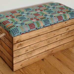 May include: A wooden storage box with a hinged lid and rope handles. The lid is upholstered with a colourful patterned fabric.