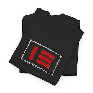 May include: Two black t-shirts are neatly folded, with one on top. The top shirt features a white rectangular outline with a red, scribbled design inside. The design consists of a vertical line and three horizontal lines.