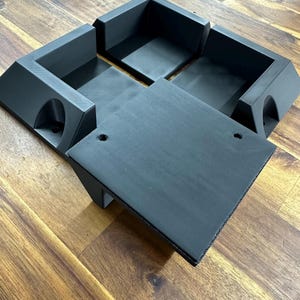 Peut inclure: Un objet en plastique noir imprimé en 3D avec quatre compartiments et une surface plane. L'objet est conçu pour contenir de petits objets, tels que des bijoux ou des outils.