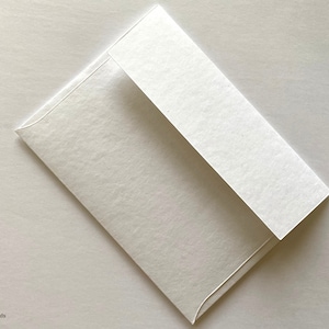 Puede incluir: Un sobre blanco con una superficie texturizada. El sobre est&aacute; doblado por la mitad y la solapa est&aacute; cerrada.