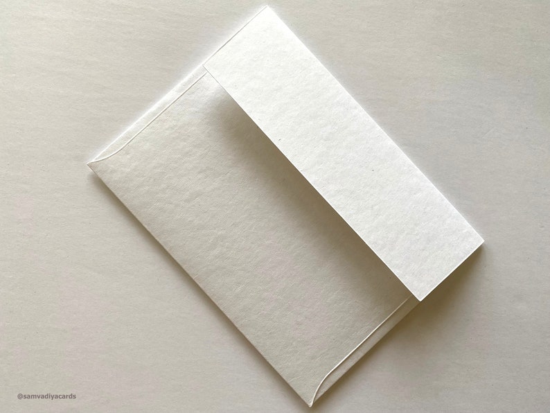 Puede incluir: Un sobre blanco con una superficie texturizada. El sobre est&aacute; doblado por la mitad y la solapa est&aacute; cerrada.
