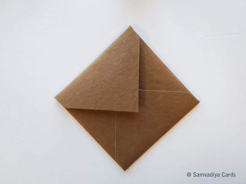 K&ouml;nnte beinhalten: Ein brauner Papierumschlag mit einer &uuml;ber die Oberseite gefalteten Klappe. Der Umschlag liegt flach auf einer wei&szlig;en Oberfl&auml;che.
