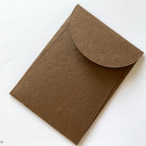 May include: A brown paper envelope with a rounded flap. The envelope is made of a textured paper.