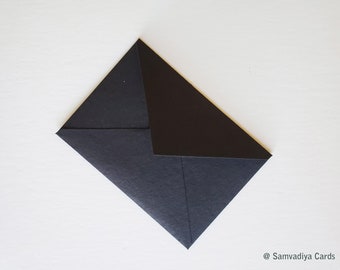 May include: A black envelope with a flap on the top. The envelope is lying flat on a white surface.