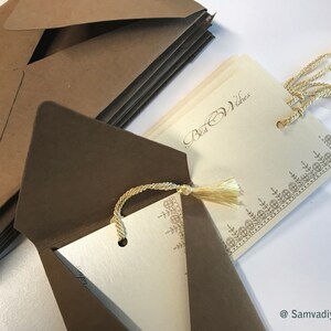 May include: A stack of brown envelopes with a gold seal on the top envelope. The envelopes are open to reveal a white card with a gold border and the text "Best Wishes". The card has a gold tassel attached to it.