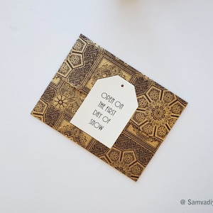 May include: A brown and gold patterned envelope with a white tag that says "Open on the first day of snow".