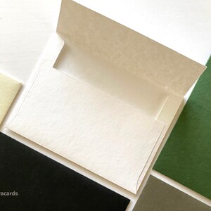 Puede incluir: Un sobre blanco con una solapa abierta, rodeado de cartulina de diferentes colores en verde, negro y crema.