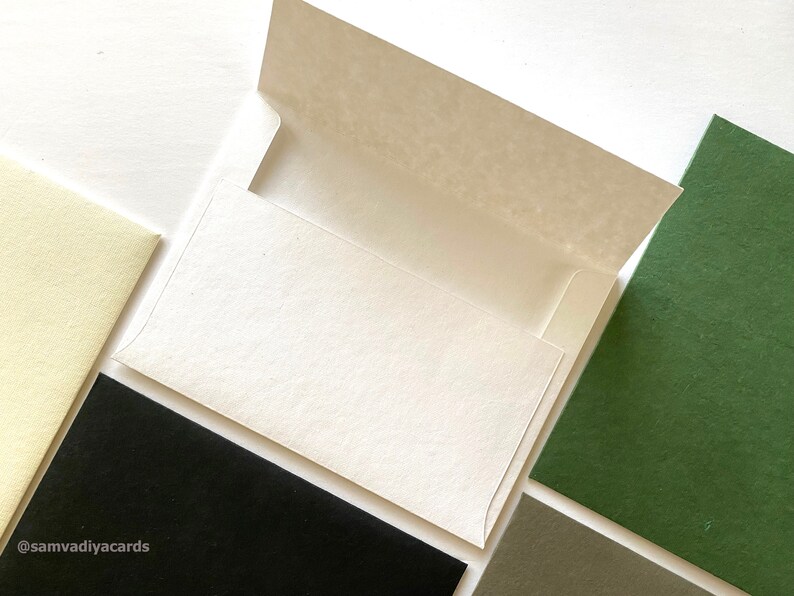 Puede incluir: Un sobre blanco con una solapa abierta, rodeado de cartulina de diferentes colores en verde, negro y crema.