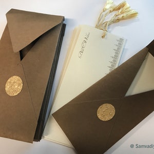 May include: A set of brown envelopes with gold foil accents and a stack of ivory cards with gold lettering and a gold tassel. The cards have the text "Best Wishes" printed on them.