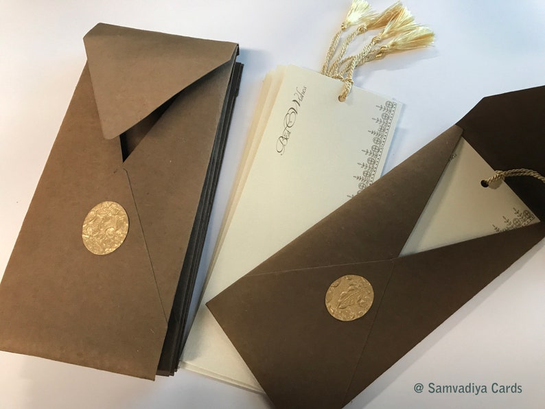 May include: A set of brown envelopes with gold foil accents and a stack of ivory cards with gold lettering and a gold tassel. The cards have the text "Best Wishes" printed on them.