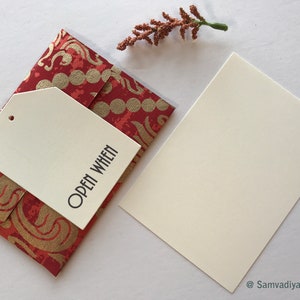 May include: A red and gold patterned envelope with a white tag attached. The tag has the text "Open When" printed on it.