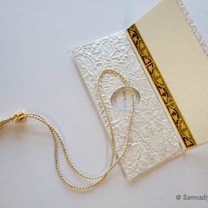 May include: White wedding invitation with a gold and burgundy border. The invitation is tied with a gold tassel.