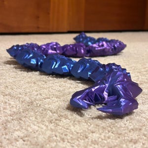 Puede incluir: Esculturas geométricas abstractas en tonos azules y morados. Los objetos tienen una apariencia facetada y cristalina, con ángulos agudos y superficies reflectantes. Las esculturas están dispuestas sobre una alfombra de color neutro, creando un contraste.