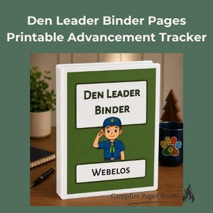 May include: A white three-ring binder with a green cover insert featuring the text Den Leader Binder and Webelos. The design includes a cartoon illustration of a scout in a blue uniform saluting. The binder is displayed on a wooden surface.