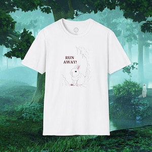 Puede incluir: Camiseta blanca con un gráfico de un conejo blanco en un entorno de bosque. El texto "RUN AWAY!" está impreso sobre el conejo.