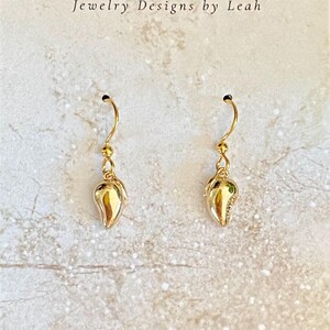 May include: A pair of gold mango-shaped dangle earrings. The earrings are on a white background with the text "Mangomia Jewelry Designs by Leah".