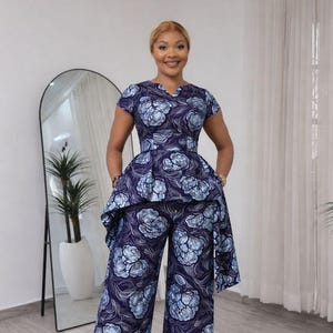 Puede incluir: Conjunto de dos piezas azul marino con estampado floral. El conjunto incluye un top de manga corta con detalle de peplum y pantalones de pernera ancha. El estampado floral es en tonos azul claro y blanco.