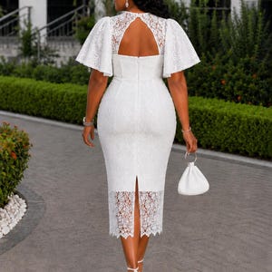 May include: A white midi-length dress featuring intricate lace detailing, short flutter sleeves, and a keyhole back cutout. The garment includes a fitted bodice, a straight skirt with a back slit, and a scalloped lace hemline, paired with a small white handbag.
