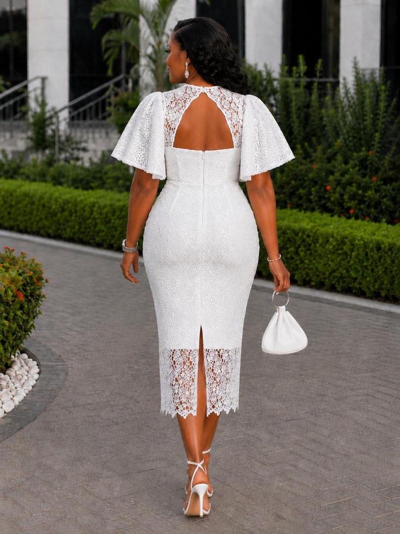 May include: A white midi-length dress featuring intricate lace detailing, short flutter sleeves, and a keyhole back cutout. The garment includes a fitted bodice, a straight skirt with a back slit, and a scalloped lace hemline, paired with a small white handbag.