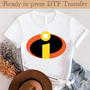 May include: White t-shirt featuring a colorful graphic design. The design includes a black oval with an orange border, a yellow 'I' shape, and a yellow circle. The text "Ready to press DTF Transfer" is at the top.