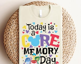 Peut inclure: Un t-shirt beige avec un motif graphique coloré qui dit "Today is a CORE MEMORY Day" avec une tête de Mickey Mouse au milieu du mot "CORE". Le graphique comprend également cinq personnages du film Vice-Versa.