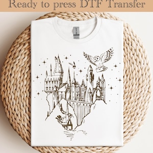 May include: White t-shirt featuring a brown graphic of a castle, an owl with a letter, and the text "Ready to press DTF Transfer". The design includes stars and a flying object. The shirt is on a woven surface.