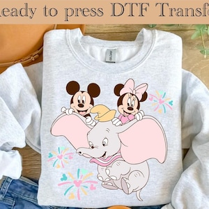 May include: A gray sweatshirt with a DTF transfer design featuring Mickey Mouse and Minnie Mouse riding Dumbo the elephant. The design includes fireworks and hearts in pastel colors.