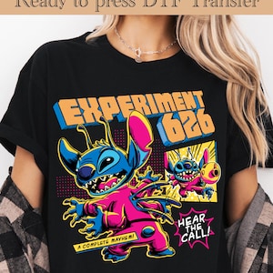 Könnte beinhalten: Schwarzes T-Shirt mit einer farbenfrohen Grafik eines blauen und rosa Alien-Charakters und dem Text "EXPERIMENT 626". Das Design enthält die Sätze "A COMPLETE MAYHEM!" und "HEAR THE CALL!" im Comic-Stil.