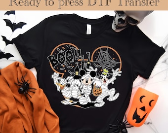 May include: Black t-shirt with a Halloween-themed design featuring Mickey Mouse, Donald Duck, and Goofy dressed as mummies. The design is in the shape of Mickey Mouse's ears with the text "Boo!" in a spooky font.