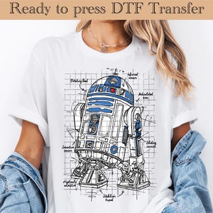 May include: White t-shirt featuring a detailed blueprint-style illustration of a robot in blue and white. The text "Ready to press DTF Transfer" is at the top. The robot design includes labels like "Rotating head" and "Infrared sensors".