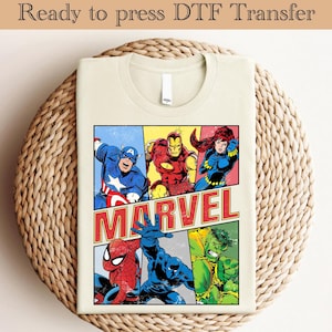 Może przedstawiać: Beżowa koszulka z nadrukiem w stylu vintage komiksu Marvela. Projekt zawiera Kapitana Amerykę, Iron Mana, Czarną Wdowę, Spider-Mana, Czarną Panterę i Hulka. Projekt jest w wielokolorowym stylu komiksowym z napisem "MARVEL" czerwonymi literami.
