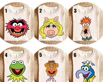 Pode incluir: Seis camisetas creme com desenhos de personagens dos Muppets. Os desenhos incluem Animal, Miss Piggy, Beaker, Kermit the Frog, Fozzie Bear e Gonzo. O texto "Ready to press DTF Transfer" está no topo.