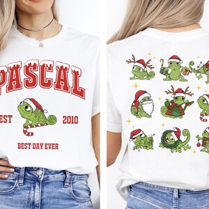 Könnte beinhalten: Weißes T-Shirt mit dem Namen "PASCAL" in roten Blockbuchstaben und einem grünen Chamäleon mit Weihnachtsmütze. Das Shirt hat auch den Text "EST 2010" und "BEST DAY EVER". Auf der Rückseite des Shirts befinden sich mehrere grüne Chamäleons mit Weihnachtsmützen.