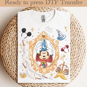 May include: White t-shirt featuring a colorful graphic of Mickey Mouse in a wizard costume inside a gold frame. The design includes the text "Ready to press DTF Transfer" at the top, and other Disney-themed elements.