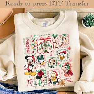 May include: Cream sweatshirt with a festive Christmas design. The graphic includes Disney characters in Santa hats, a castle, and the word "Merry". The text "Ready to press DTF Transfer" is at the top of the image.