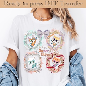 May include: White t-shirt featuring a colorful graphic of four cartoon kittens in ornate frames. The design includes the text "Super Kitties" and the phrase "Ready to press DTF Transfer" at the top.