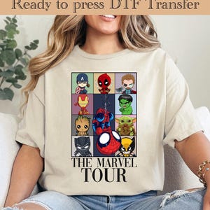 May include: A beige t-shirt with a graphic of various Marvel characters in a grid. The characters are in a cartoon style and include Spider-Man, Iron Man, Captain America, Hulk, Wolverine, Deadpool, and more. The text "THE MARVEL TOUR" is below the grid.