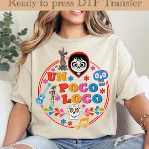 May include: Beige t-shirt featuring a colorful "Un Poco Loco" design with a skull, dog, guitar, and floral elements. The text "Ready to press DTF Transfer" is at the top. The design is in red, blue, orange, and green.