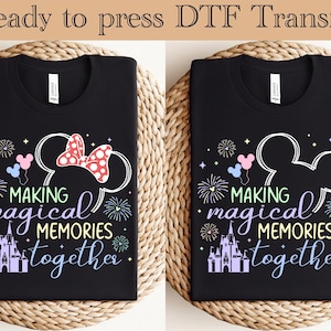 May include: Two black t-shirts with a colorful graphic design. The design includes Mickey Mouse ears, a bow, fireworks, a castle, and the text "Making magical memories together."
